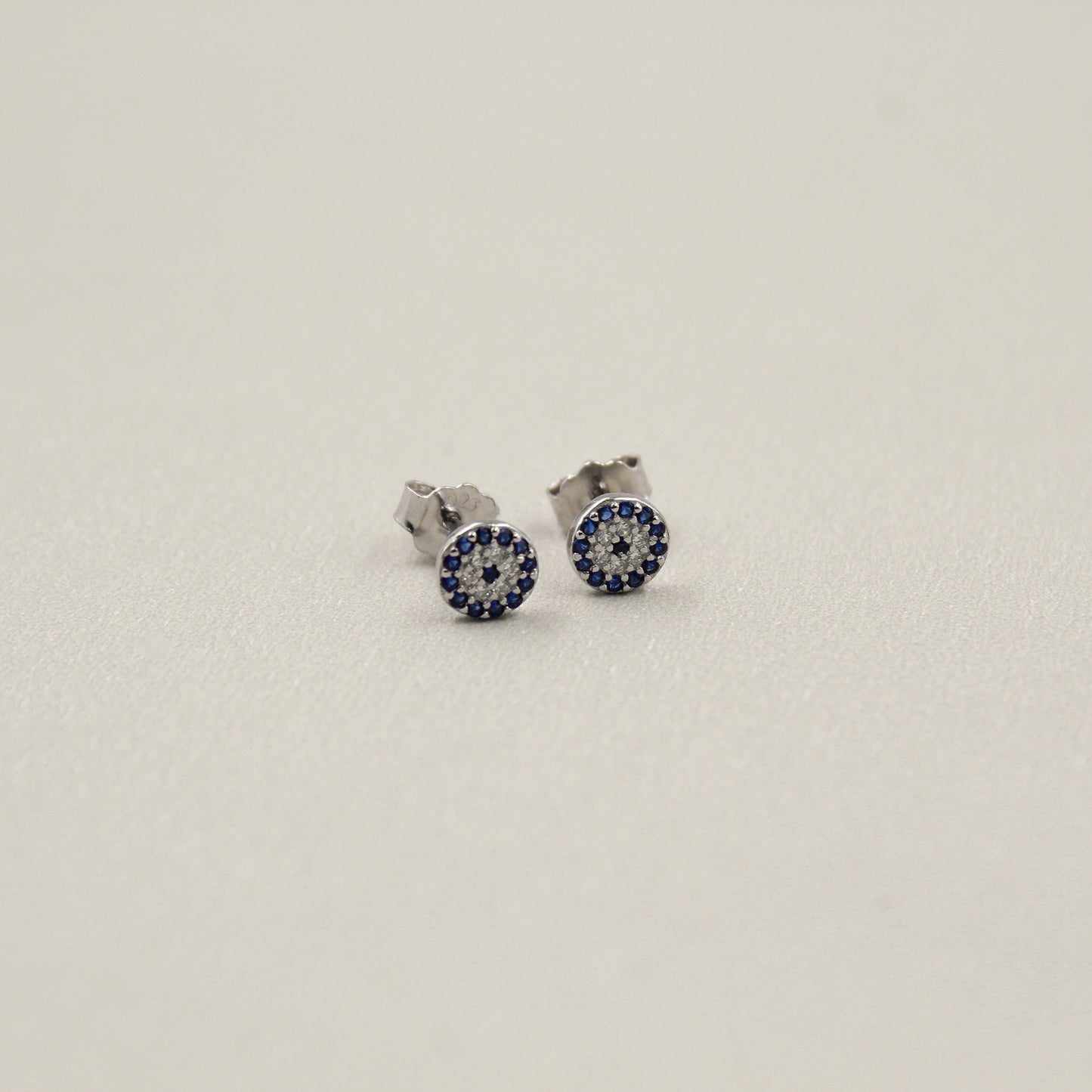 Pendientes pequeños de plata con incrustaciones de piedras azules en diseño circular.