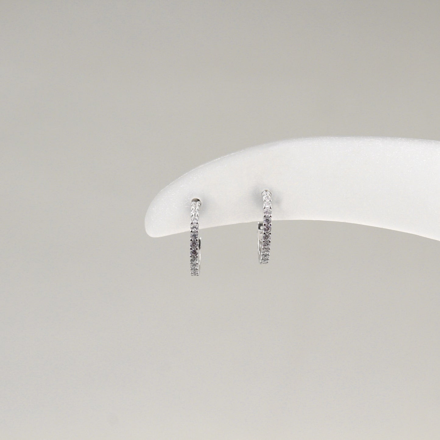 Par de aretes de aro pequeño, completamente cubiertos de diamantes, exhibidos en un soporte blanco.