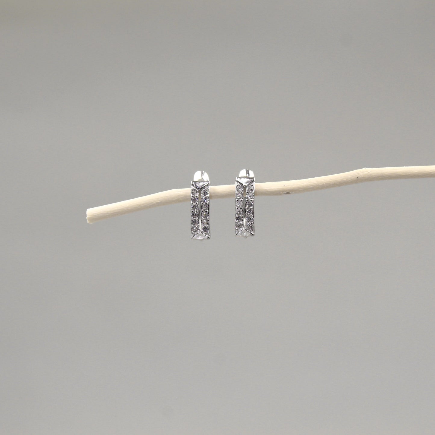 Arete de barra vertical con incrustaciones de pequeños diamantes, suspendidos de una rama delgada contra un fondo gris neutro