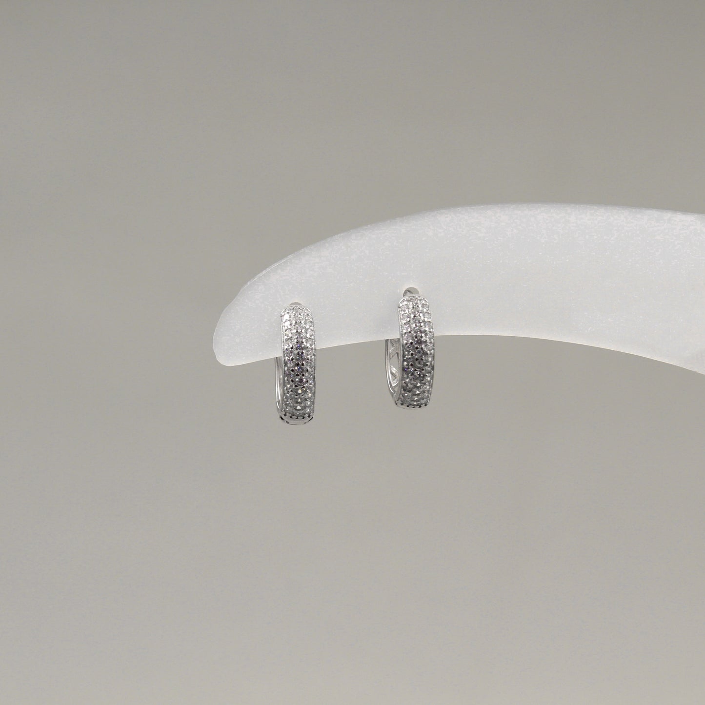 Par de aretes pequeños de aro, completamente cubiertos de diamantes, exhibidos en un soporte blanco.