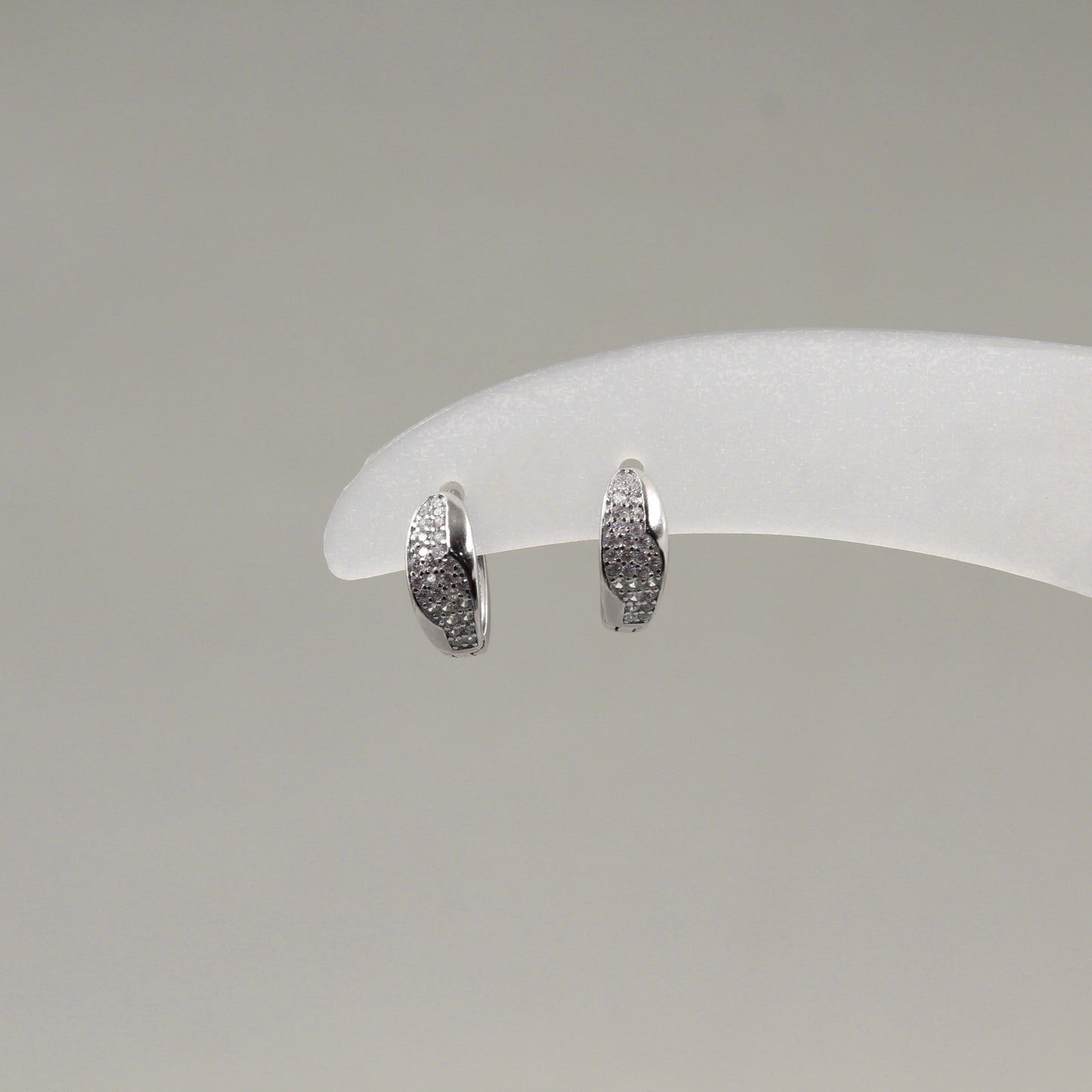 Par de aretes pequeños de aro, adornados con diamantes en un diseño ondulado, exhibidos en un soporte blanco.