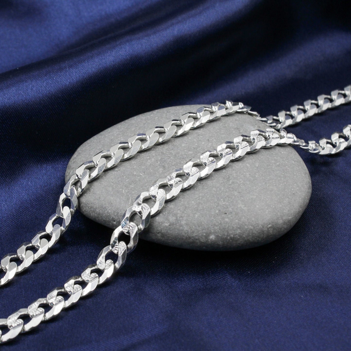 Cadena de plata con eslabones cubanos de doble vista sobre una superficie de piedra.