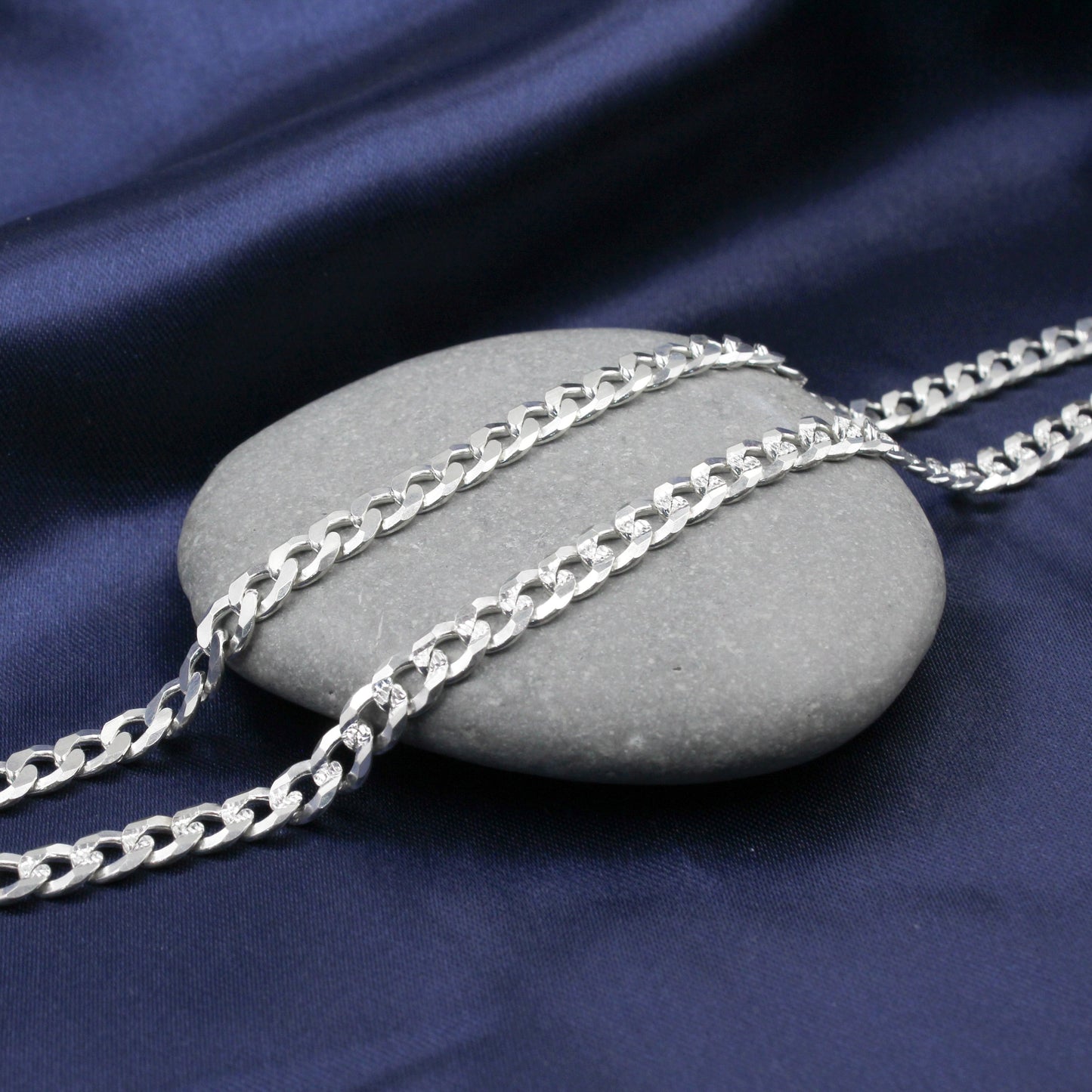 Cadena de plata con eslabones cubanos de doble vista sobre una superficie de piedra.