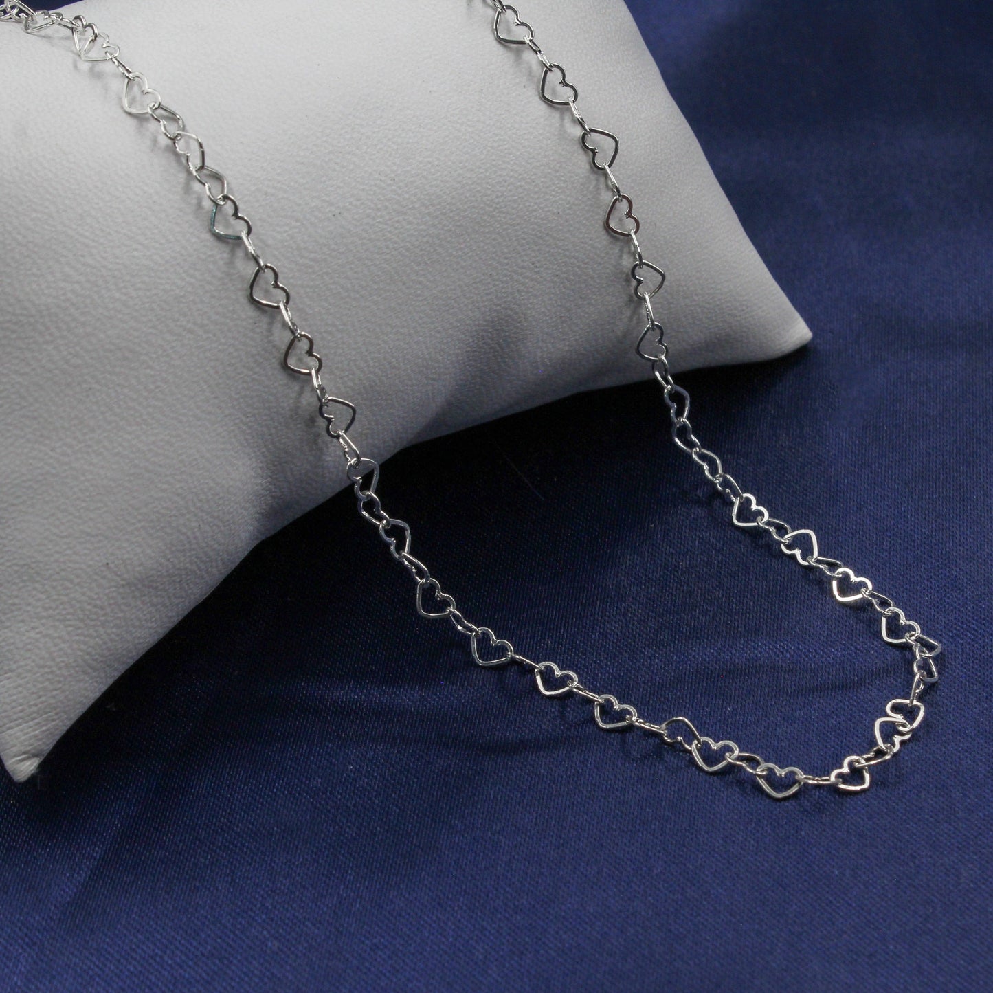 Cadena de eslabones de corazones de plata sobre cojín blanco.