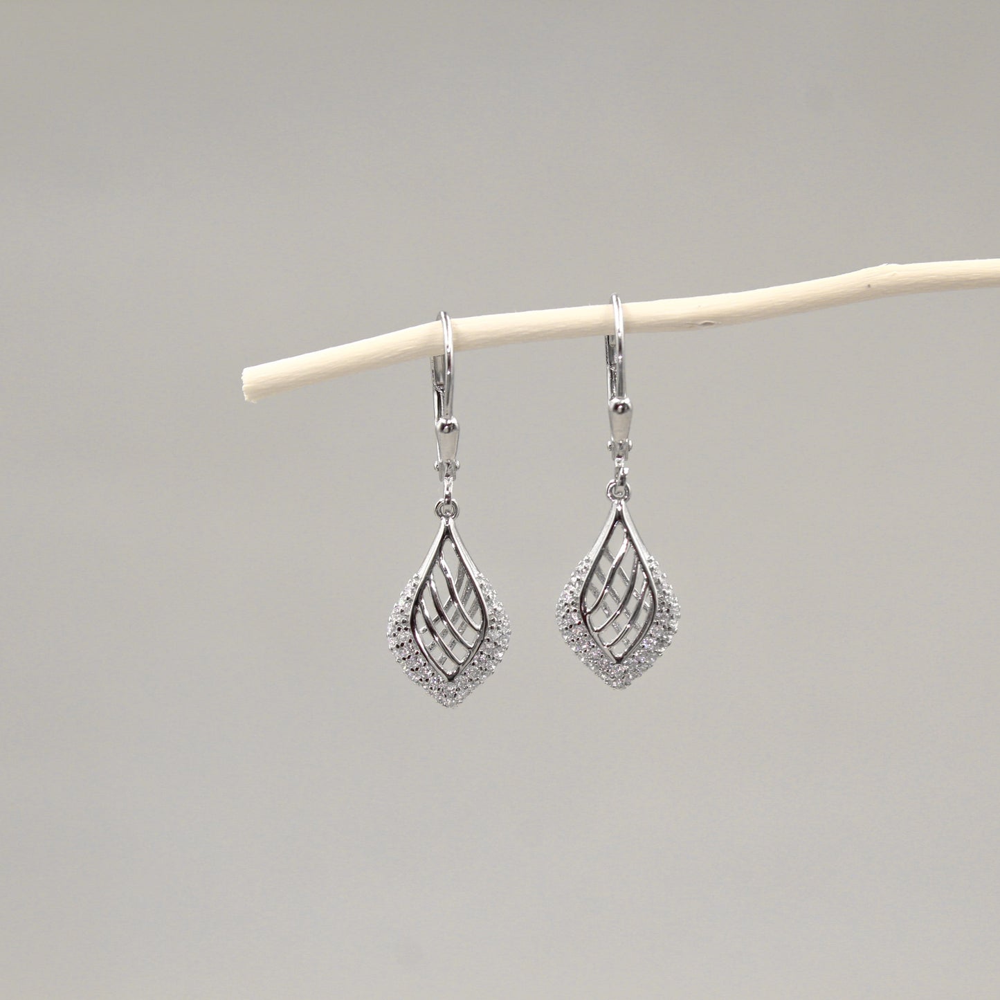 Par de aretes colgantes con diseño de hoja, adornados con diamantes, colgando de una rama blanca.