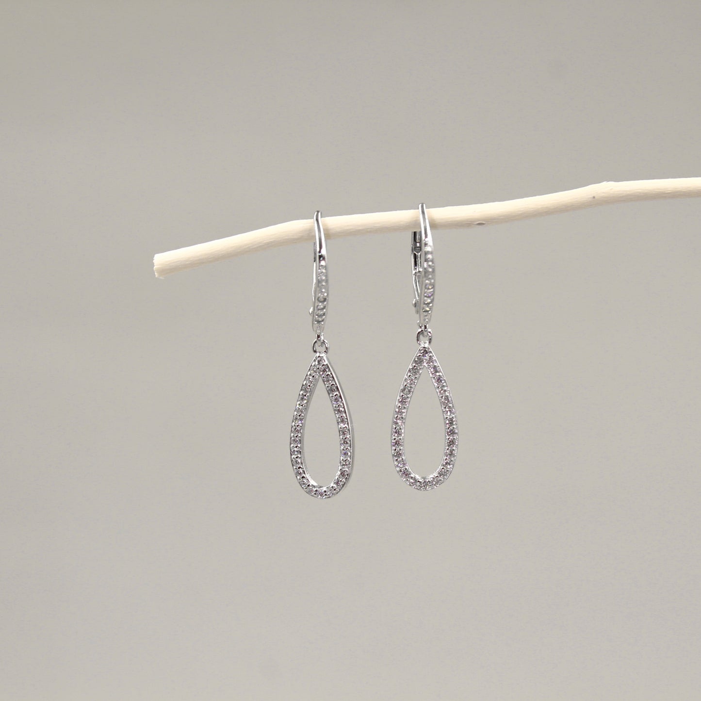 Par de aretes colgantes en forma de lágrima, adornados con diamantes, colgando de una rama blanca.