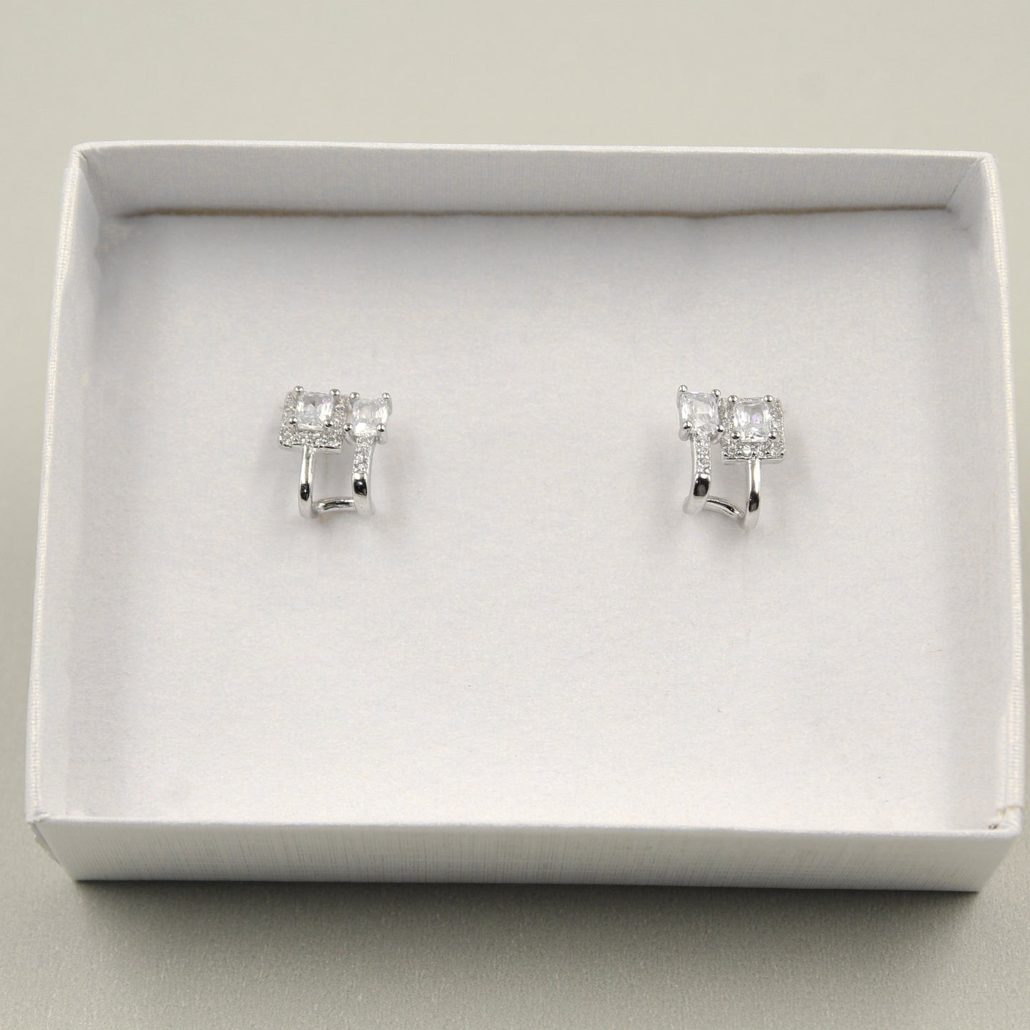 Par de aretes pequeños con diamantes rectangulares, presentados en una caja blanca.
