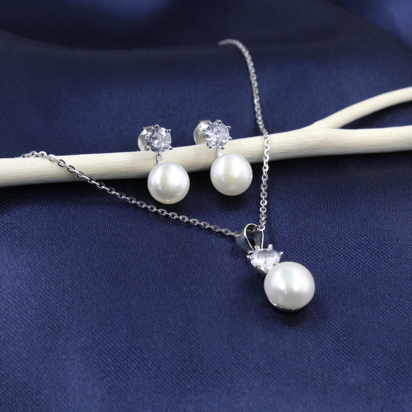 Juego de joyería con colgante, aretes con perlas y zirconias, sobre fondo de tela azul.