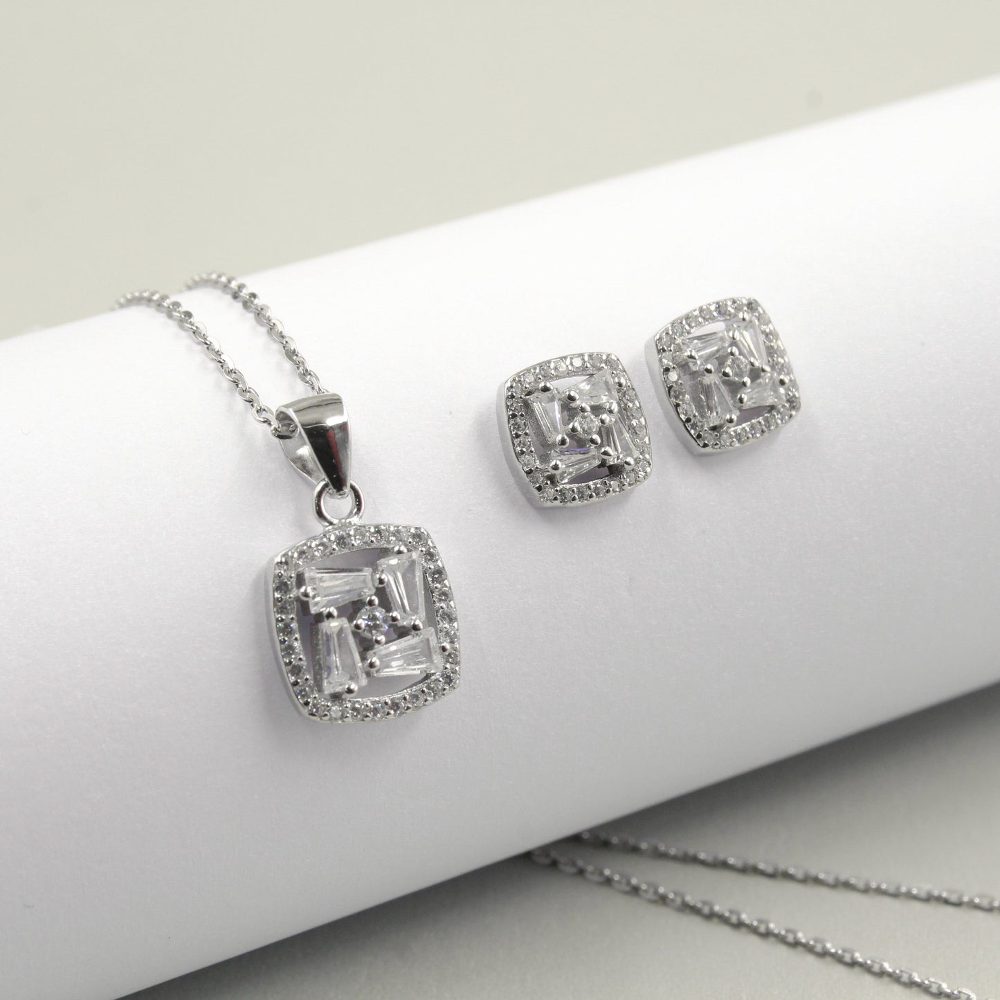 Juego de joyería con colgante y aretes cuadrados decorados con pequeños diamantes, sobre fondo blanco.