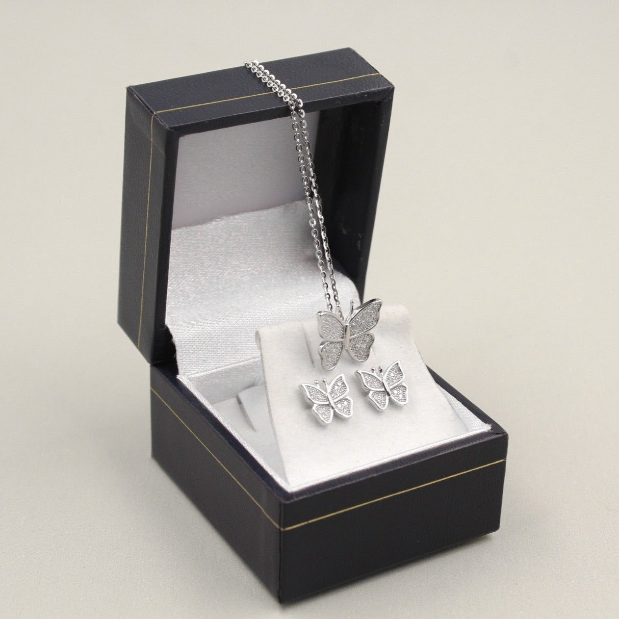 Juego de joyería con colgante y aretes en forma de mariposa, decorados con pequeños diamantes, presentados en una caja negra.
