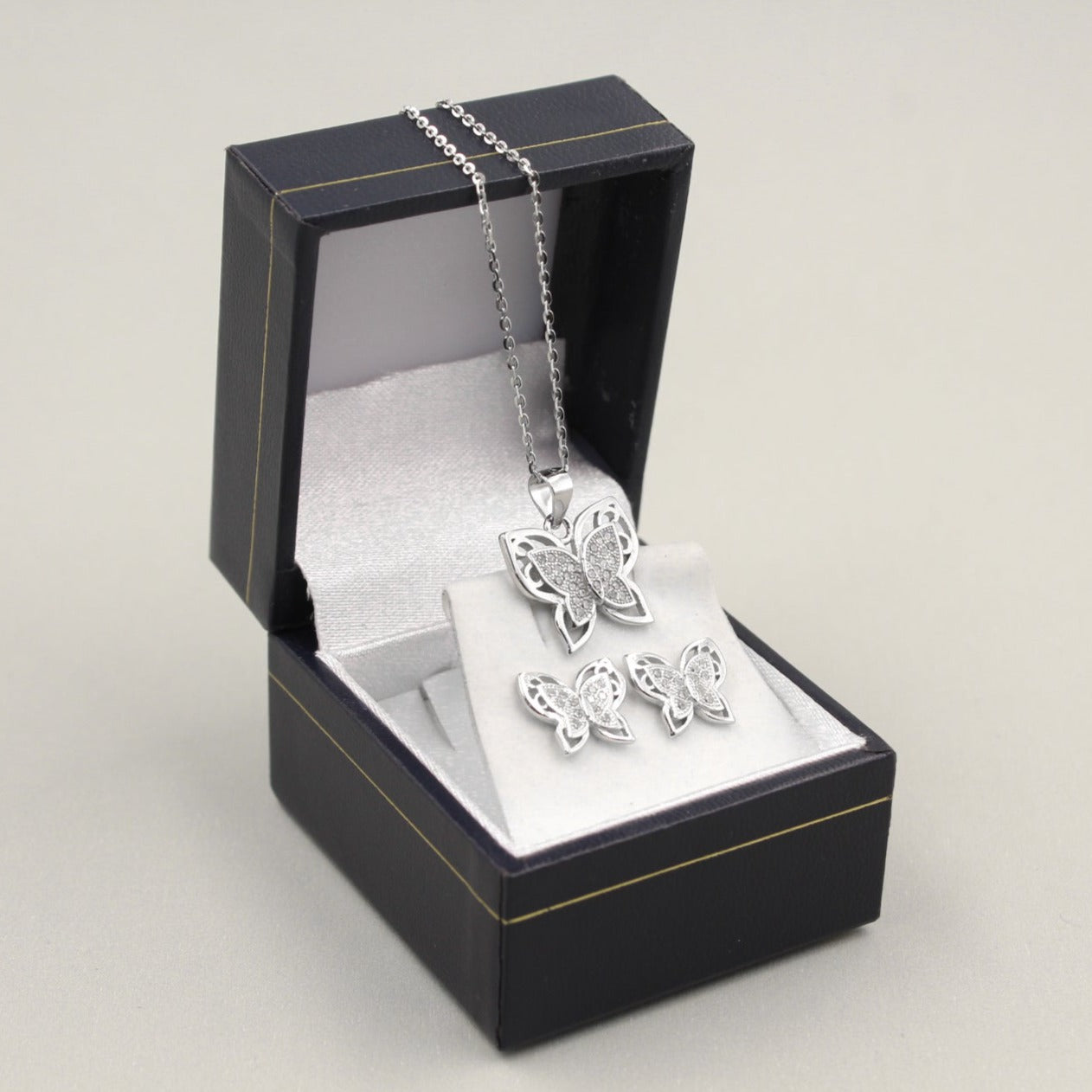 Juego de joyería con colgante y aretes en forma de mariposa, decorados con pequeños diamantes, presentados en una caja negra.