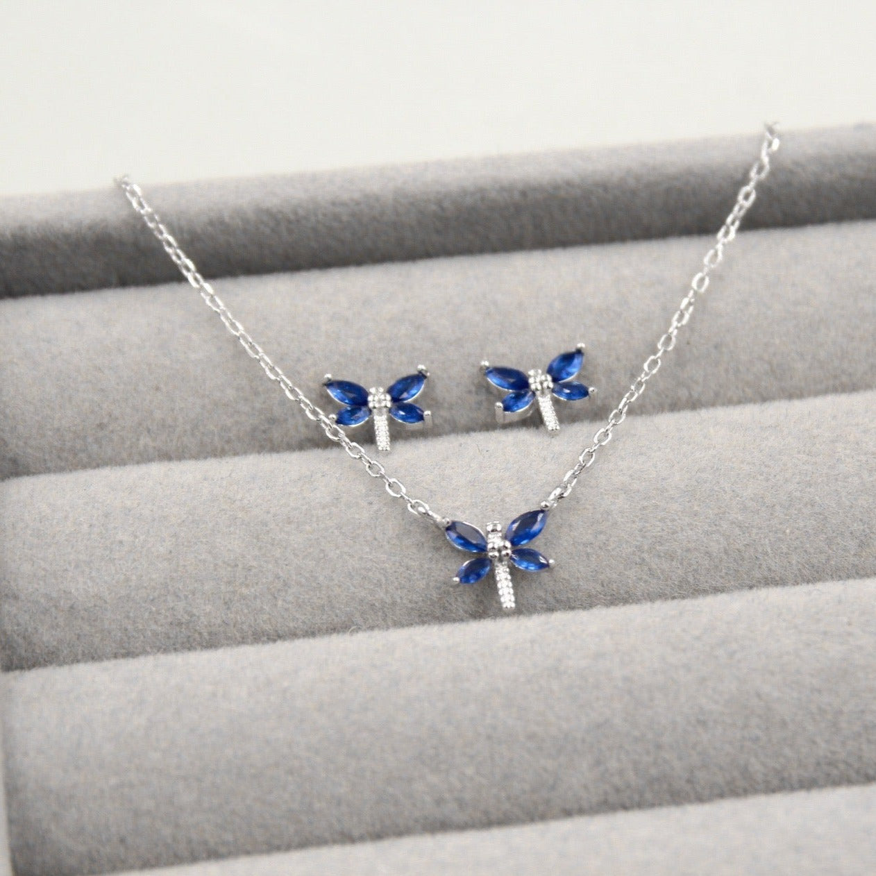 Conjunto de joyería de plata con diseño de libélulas azules, que incluye un collar y un par de aretes.