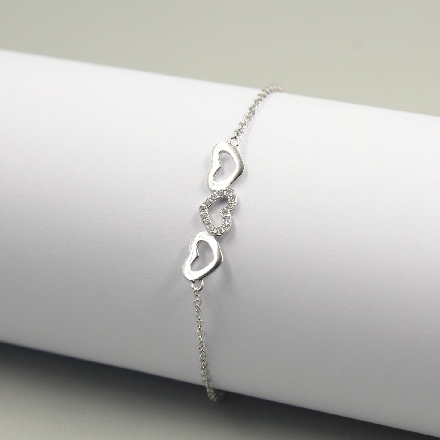 Pulsera de plata con tres dijes de corazones, uno de ellos adornado con pequeños diamantes.