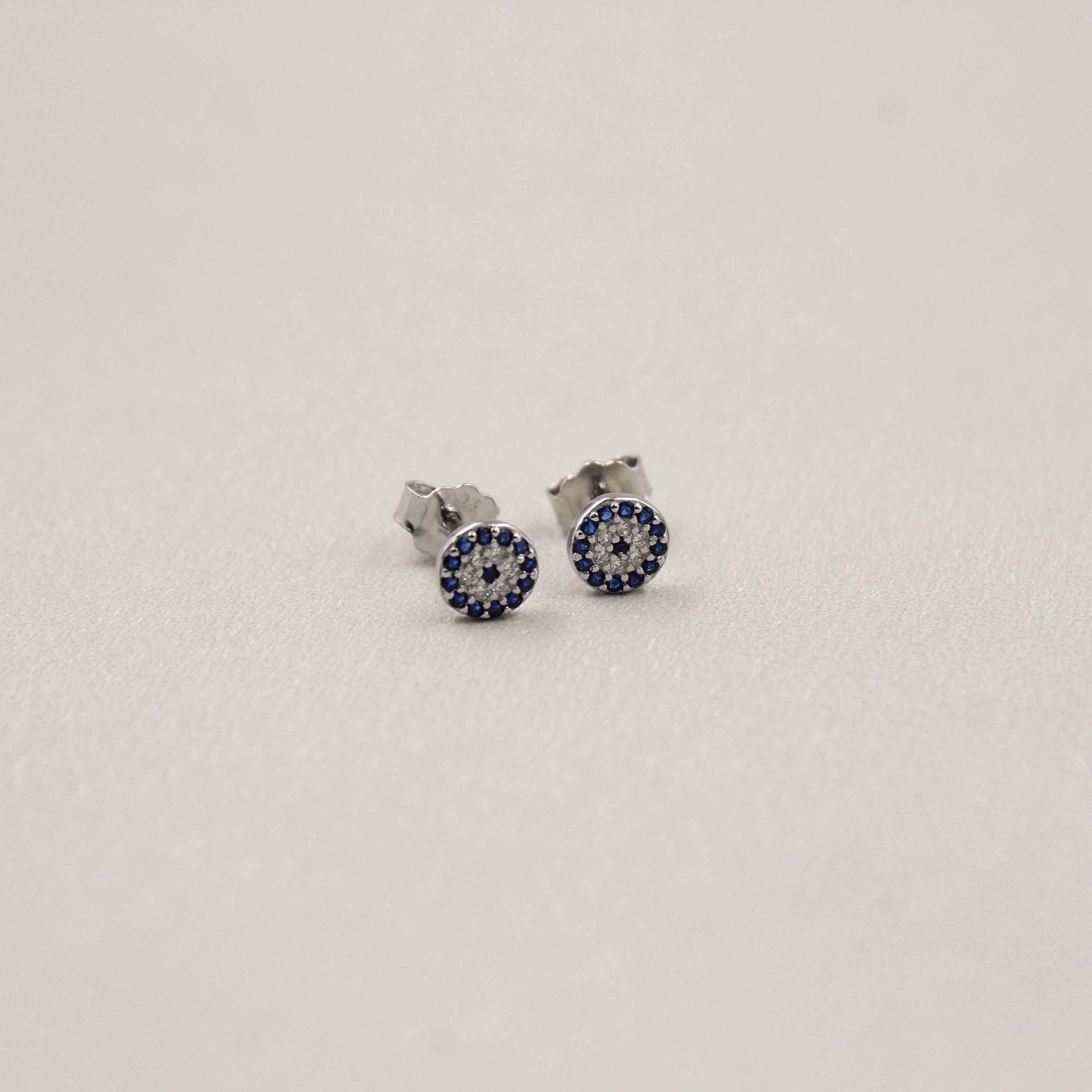 Pendientes pequeños de plata con incrustaciones de piedras azules en diseño circular.