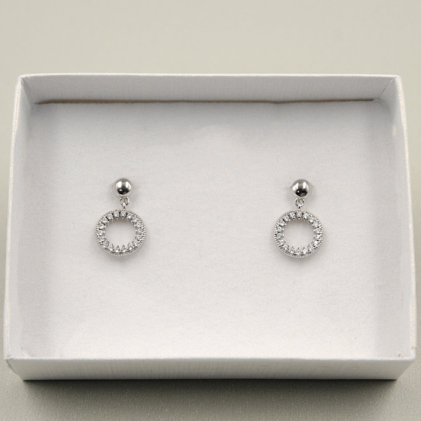 Par de aretes colgantes con un diseño circular adornado con diamantes, presentados en una caja blanca.