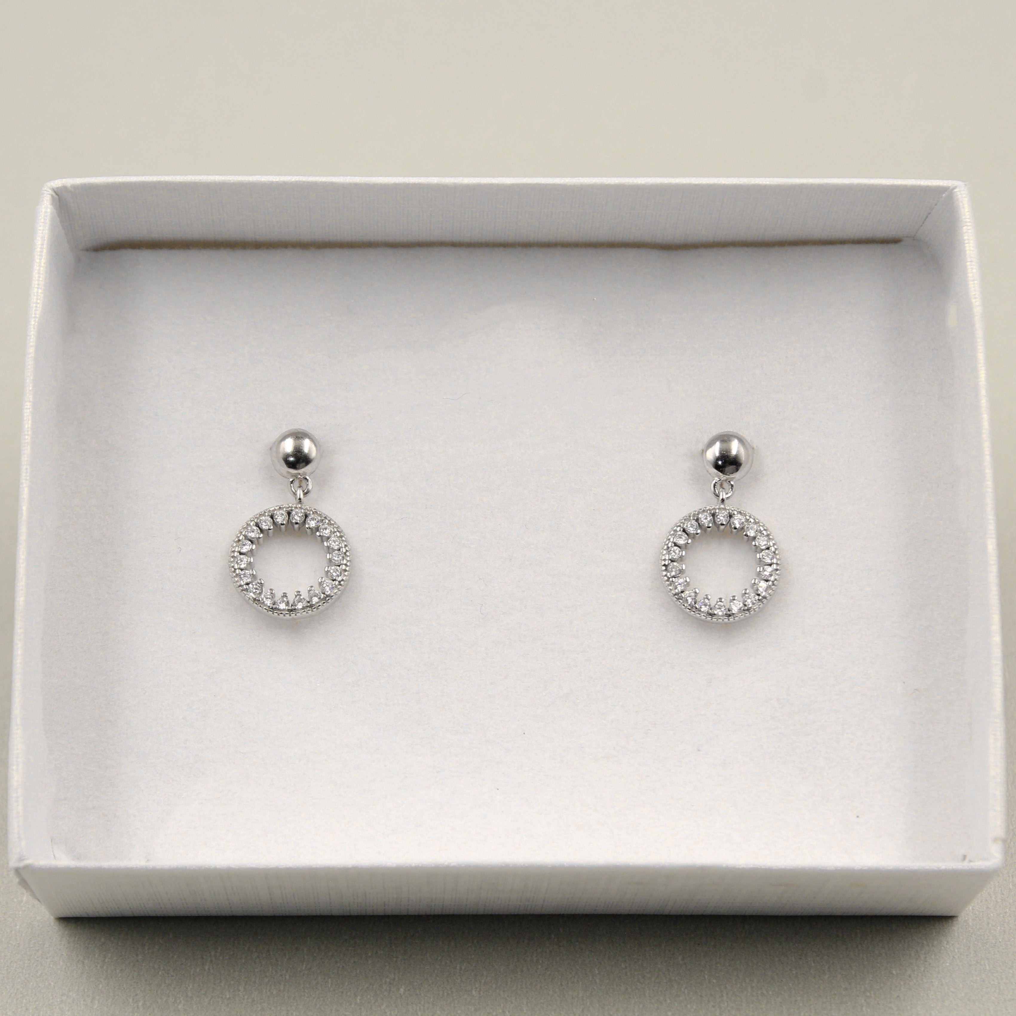 Par de aretes colgantes con un diseño circular adornado con diamantes, presentados en una caja blanca.