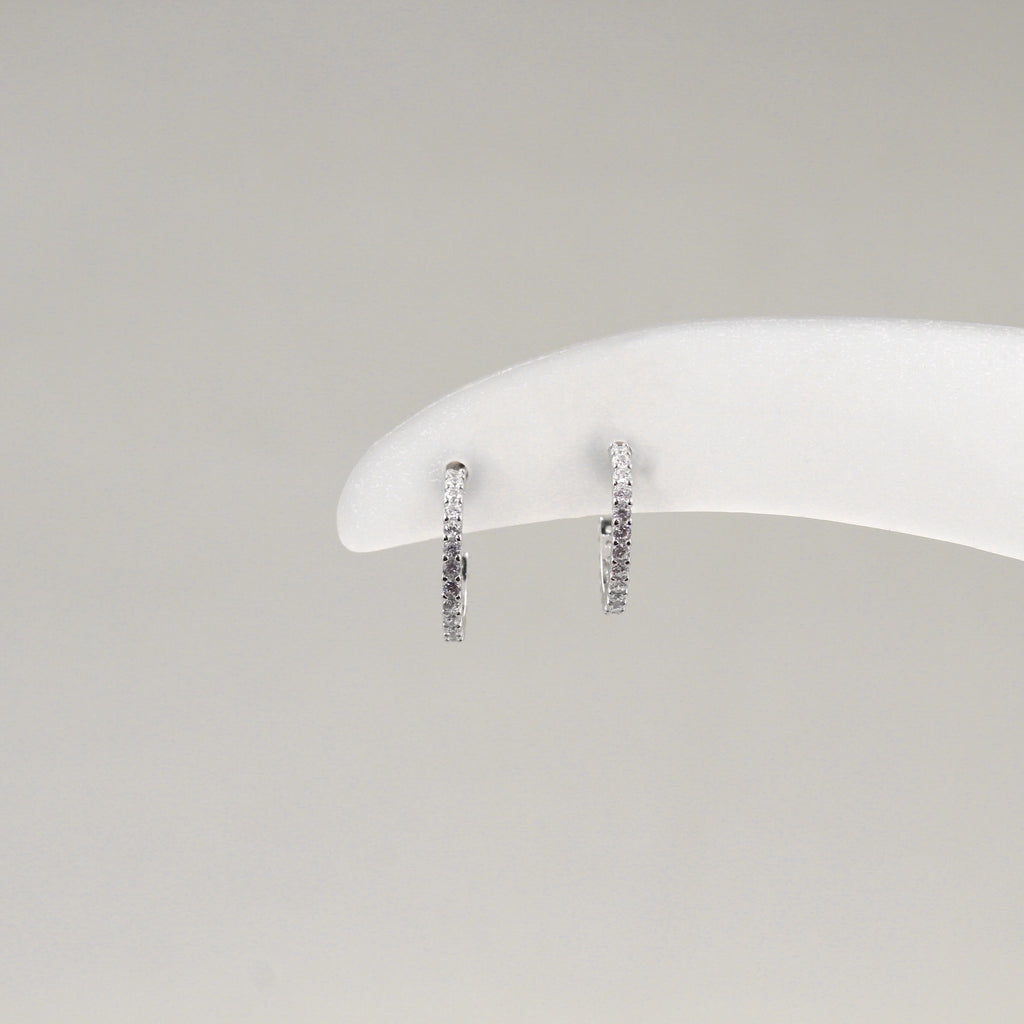 Par de aretes de aro pequeño, completamente cubiertos de diamantes, exhibidos en un soporte blanco.