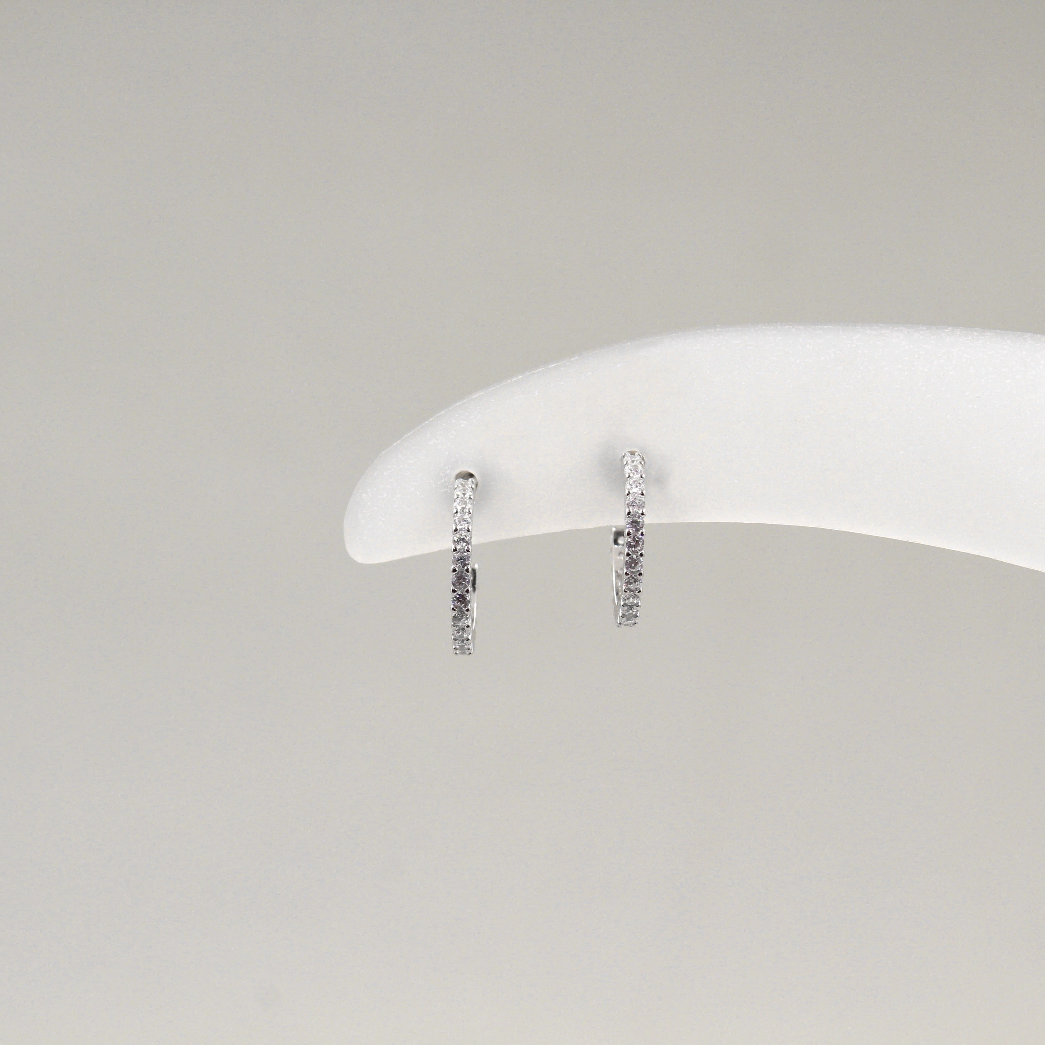 Par de aretes de aro pequeño, completamente cubiertos de diamantes, exhibidos en un soporte blanco.