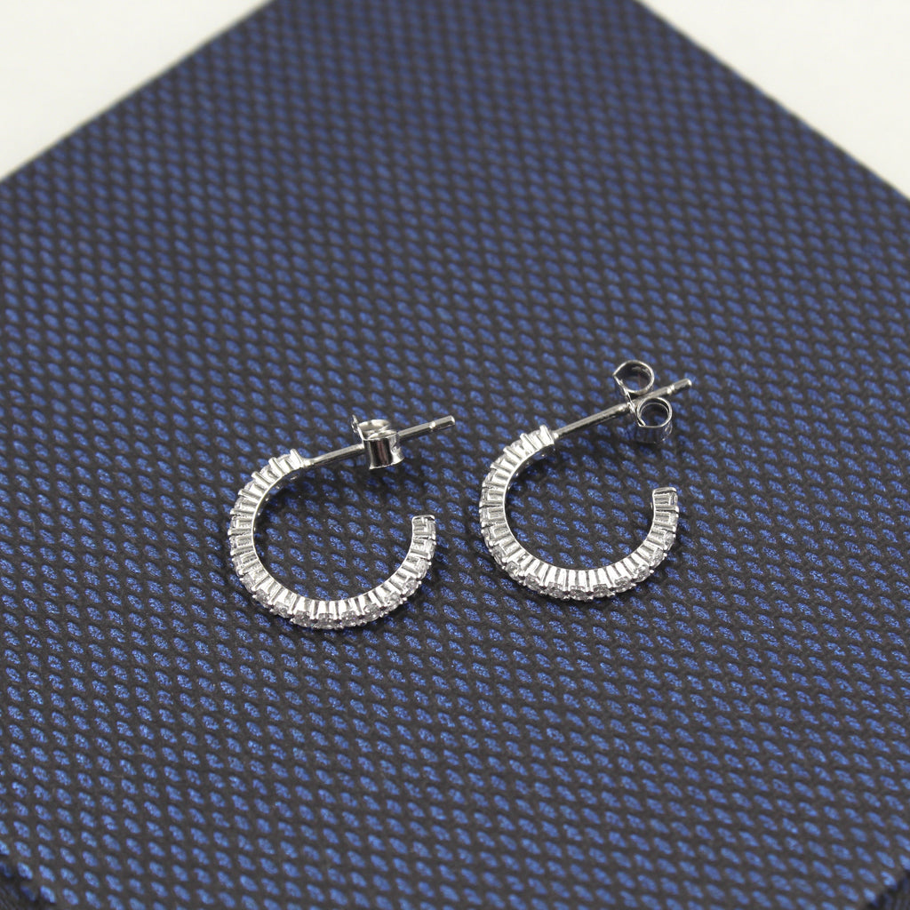 Par de aretes de aro medio, adornados con diamantes baguette, presentados sobre un fondo texturizado azul oscuro.