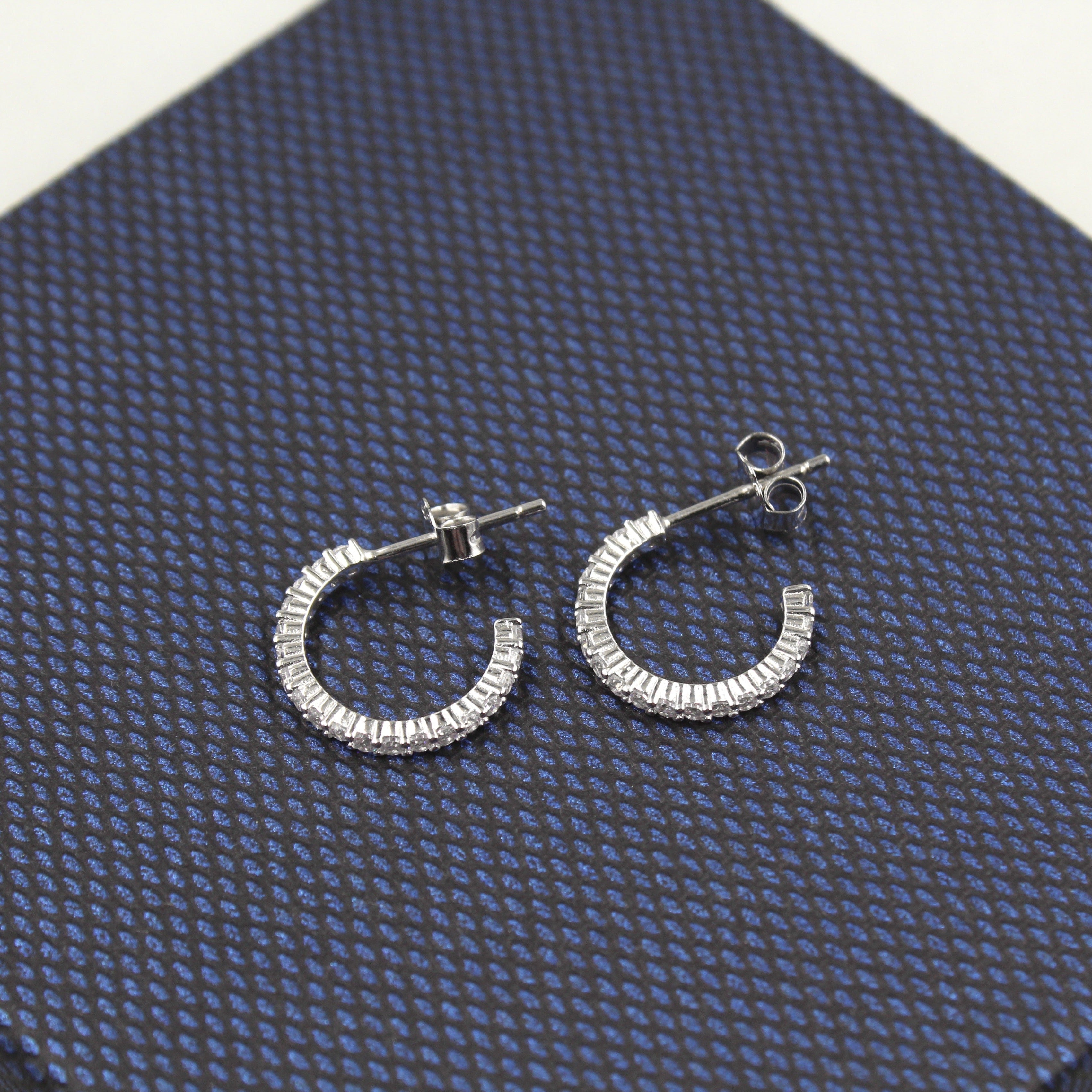 Par de aretes de aro medio, adornados con diamantes baguette, presentados sobre un fondo texturizado azul oscuro.