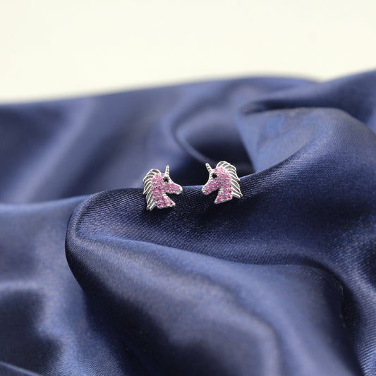 Pendientes de unicornio con piedras rosadas sobre una tela azul.