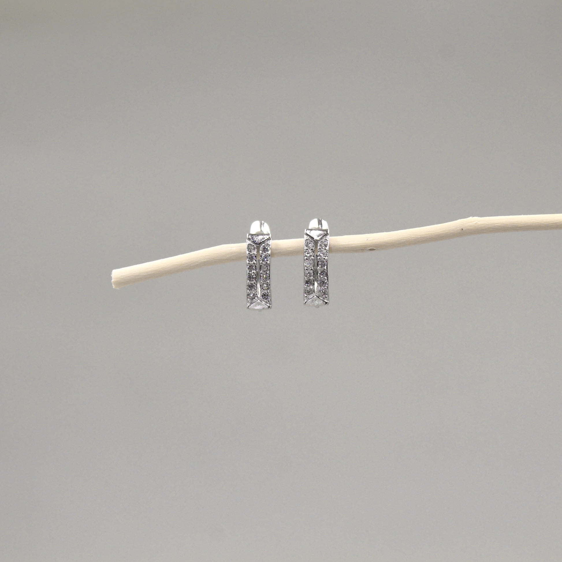 Arete de barra vertical con incrustaciones de pequeños diamantes, suspendidos de una rama delgada contra un fondo gris neutro