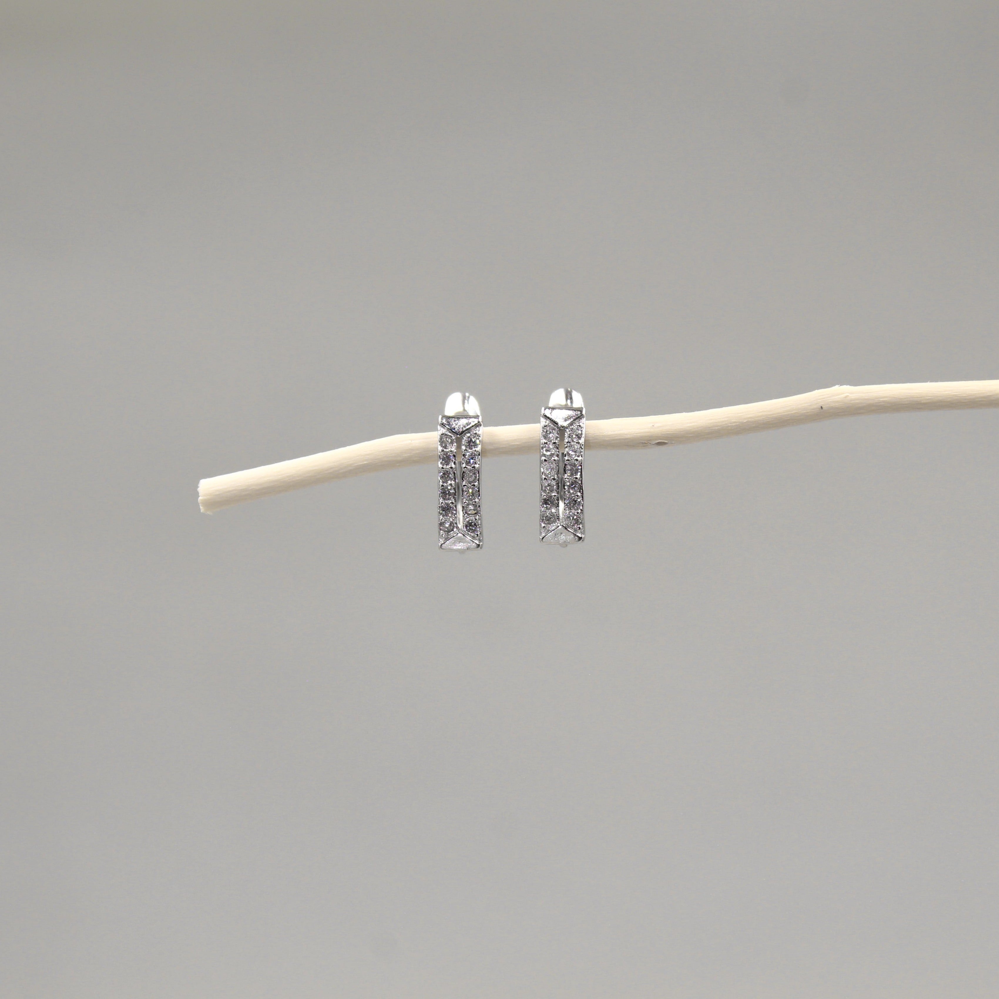 Arete de barra vertical con incrustaciones de pequeños diamantes, suspendidos de una rama delgada contra un fondo gris neutro