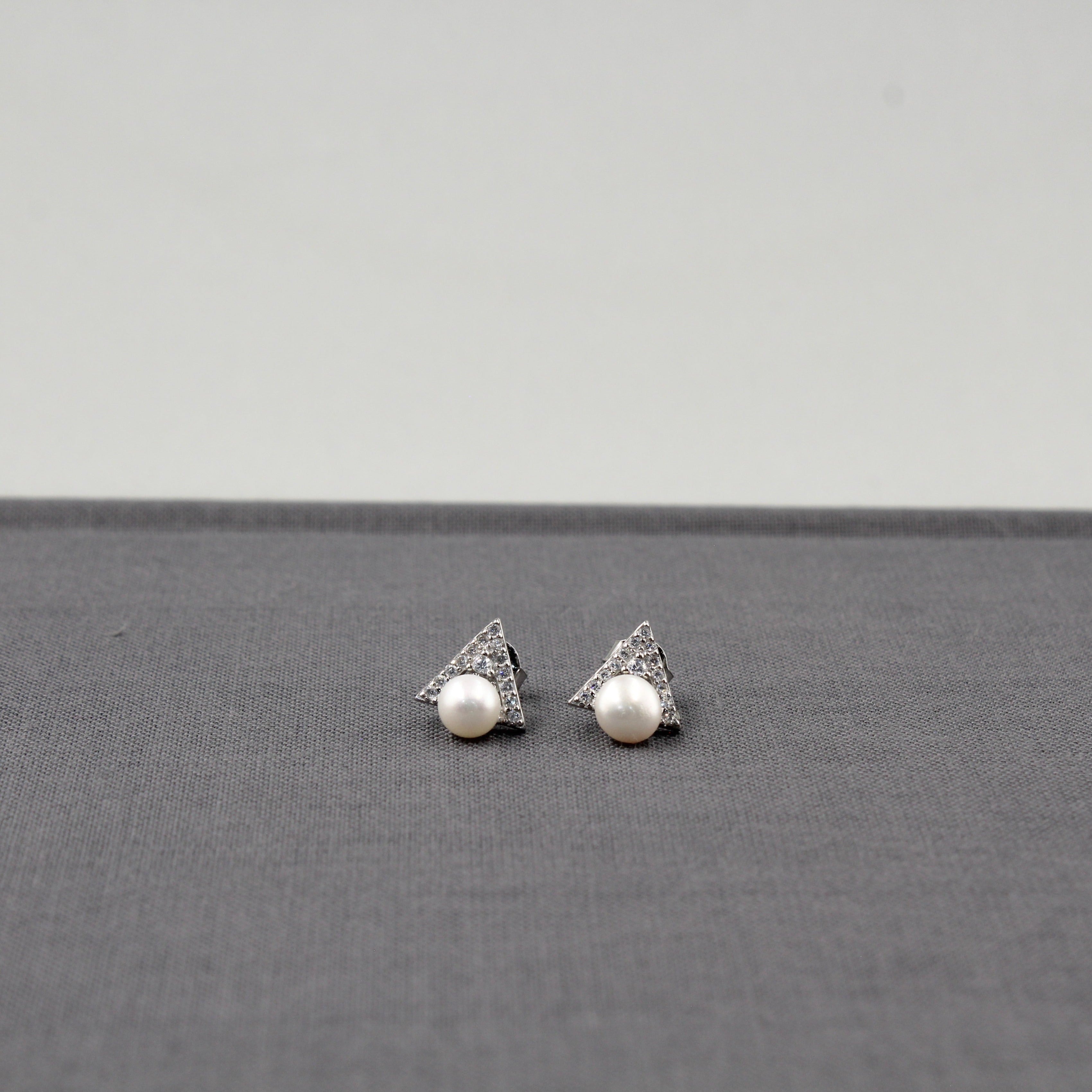 Aretes de triángulo con una perla y detalles de diamantes en miniatura, presentados sobre un fondo gris.