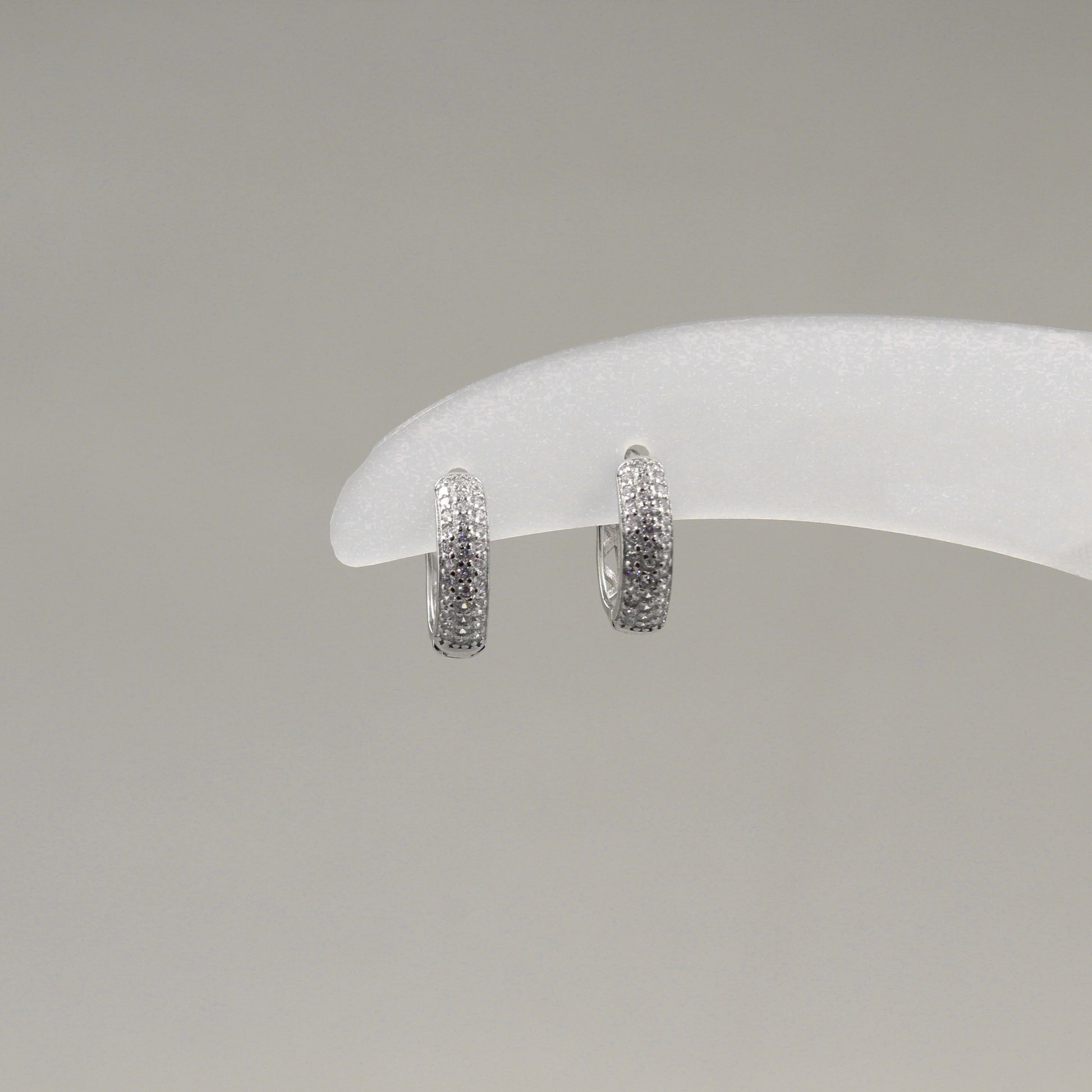 Par de aretes pequeños de aro, completamente cubiertos de diamantes, exhibidos en un soporte blanco.