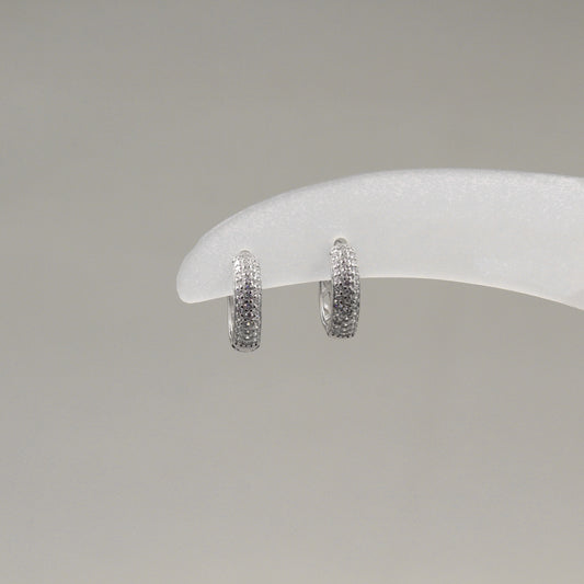 Par de aretes pequeños de aro, completamente cubiertos de diamantes, exhibidos en un soporte blanco.