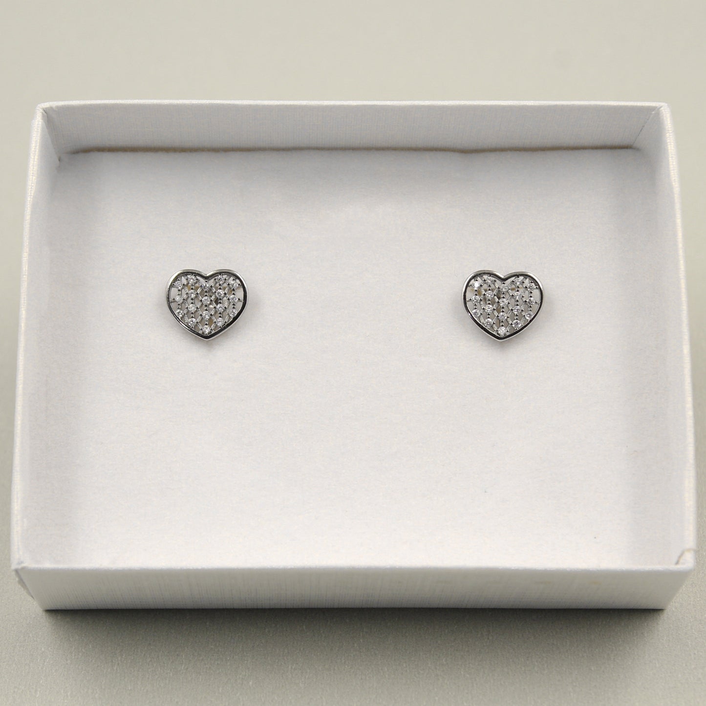 Pendientes en forma de corazón con incrustaciones de pequeños diamantes, presentados en una caja blanca.