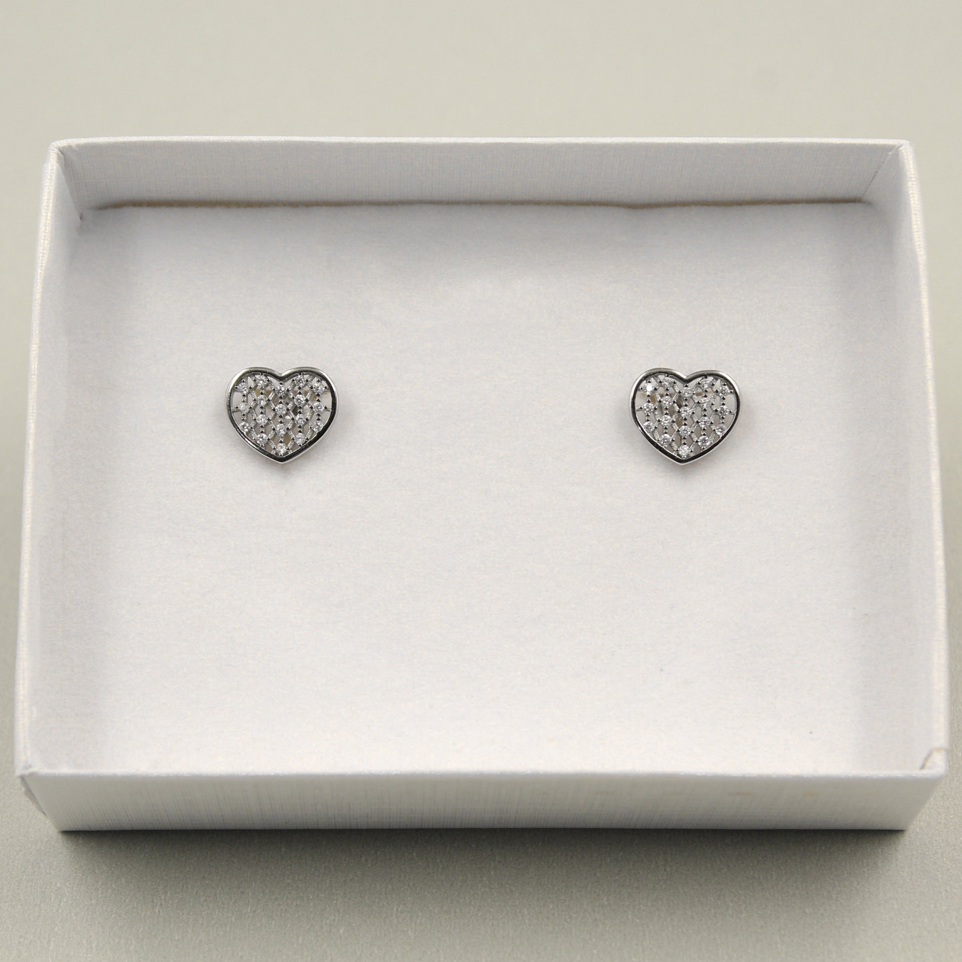 Pendientes en forma de corazón con incrustaciones de pequeños diamantes, presentados en una caja blanca.