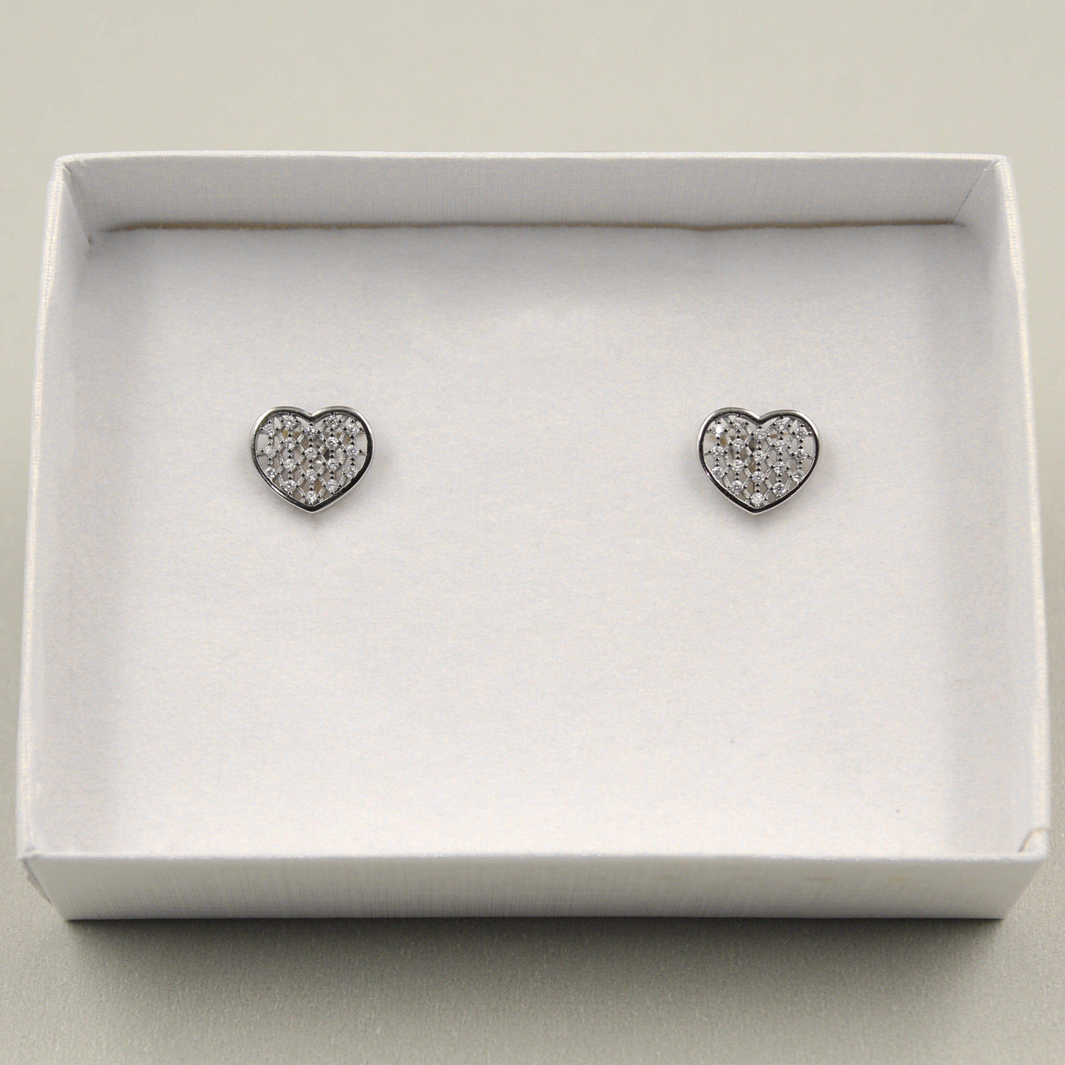 Pendientes en forma de corazón con incrustaciones de pequeños diamantes, presentados en una caja blanca.