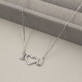 collar de plata con un colgante que forma la frase 'I ♥ U', con el corazón cubierto de pequeñas circonias cúbicas brillantes. El collar se presenta sobre un fondo gris suave con líneas horizontales, complementando el brillo del colgante.