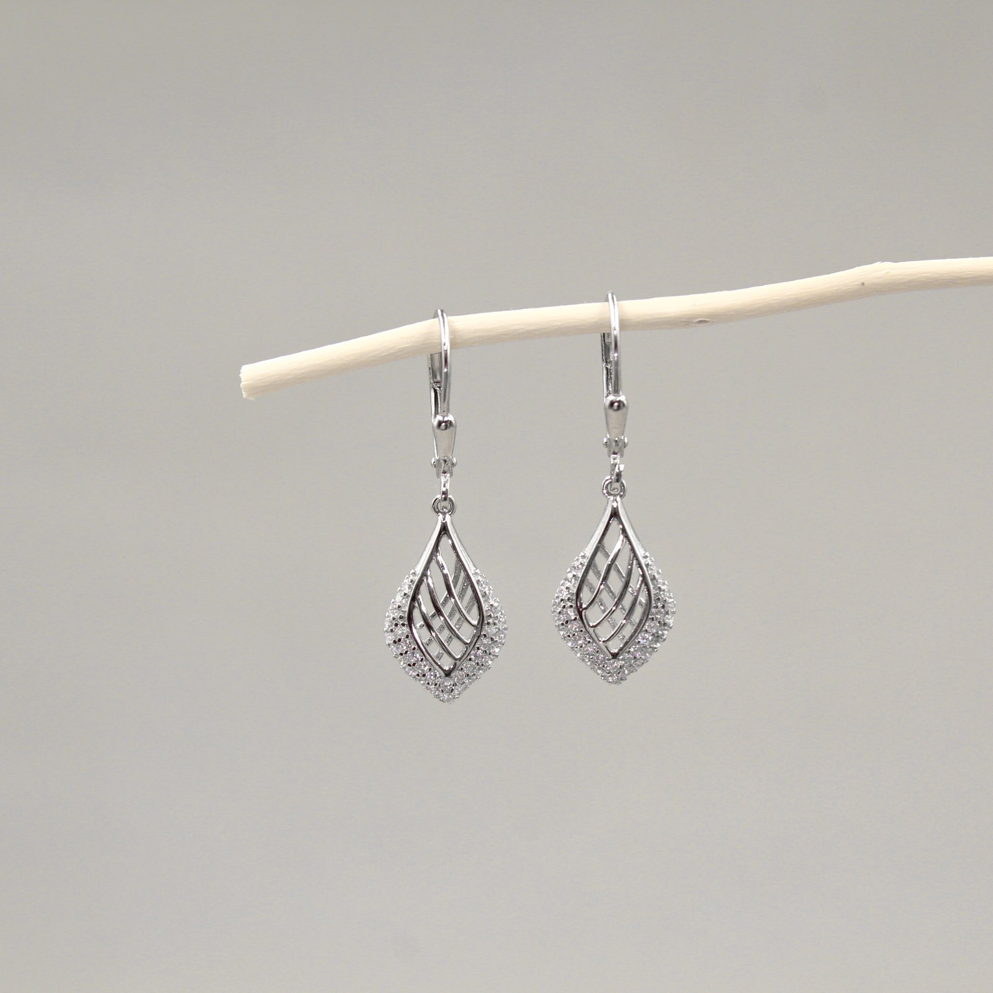 Par de aretes colgantes con diseño de hoja, adornados con diamantes, colgando de una rama blanca.