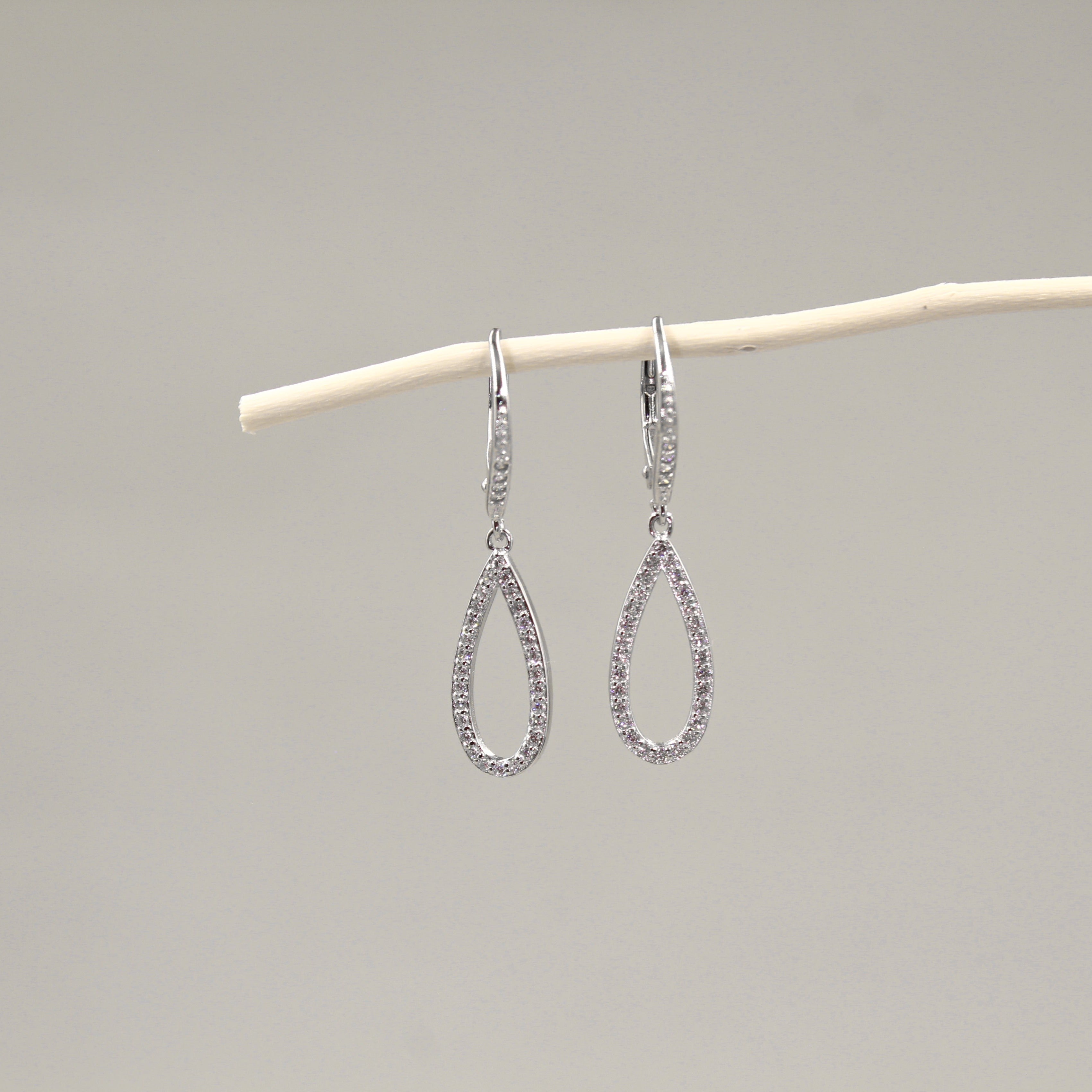 Par de aretes colgantes en forma de lágrima, adornados con diamantes, colgando de una rama blanca.