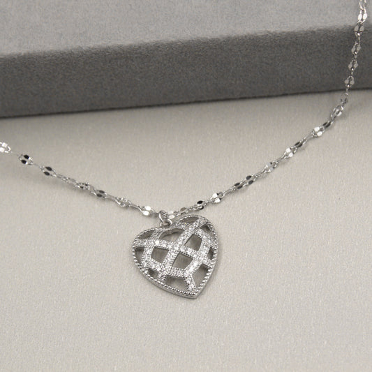 collar de plata con un colgante en forma de corazón que tiene un diseño de rejilla. El corazón está detalladamente adornado con circonias cúbicas a lo largo de las líneas de la rejilla, creando un patrón brillante y atractivo. El collar se presenta sobre un fondo gris con una caja de regalo al fondo.