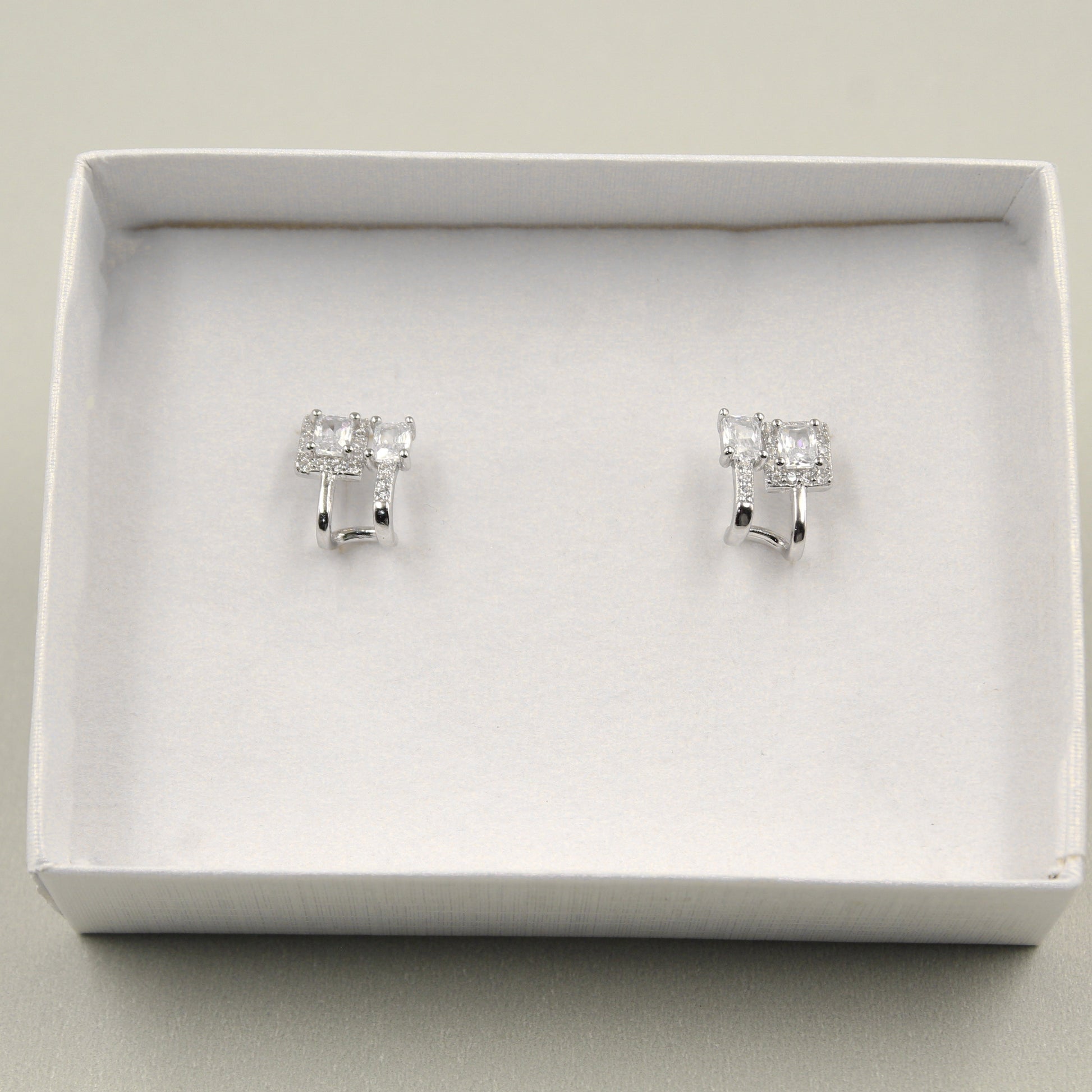 Par de aretes pequeños con diamantes rectangulares, presentados en una caja blanca.
