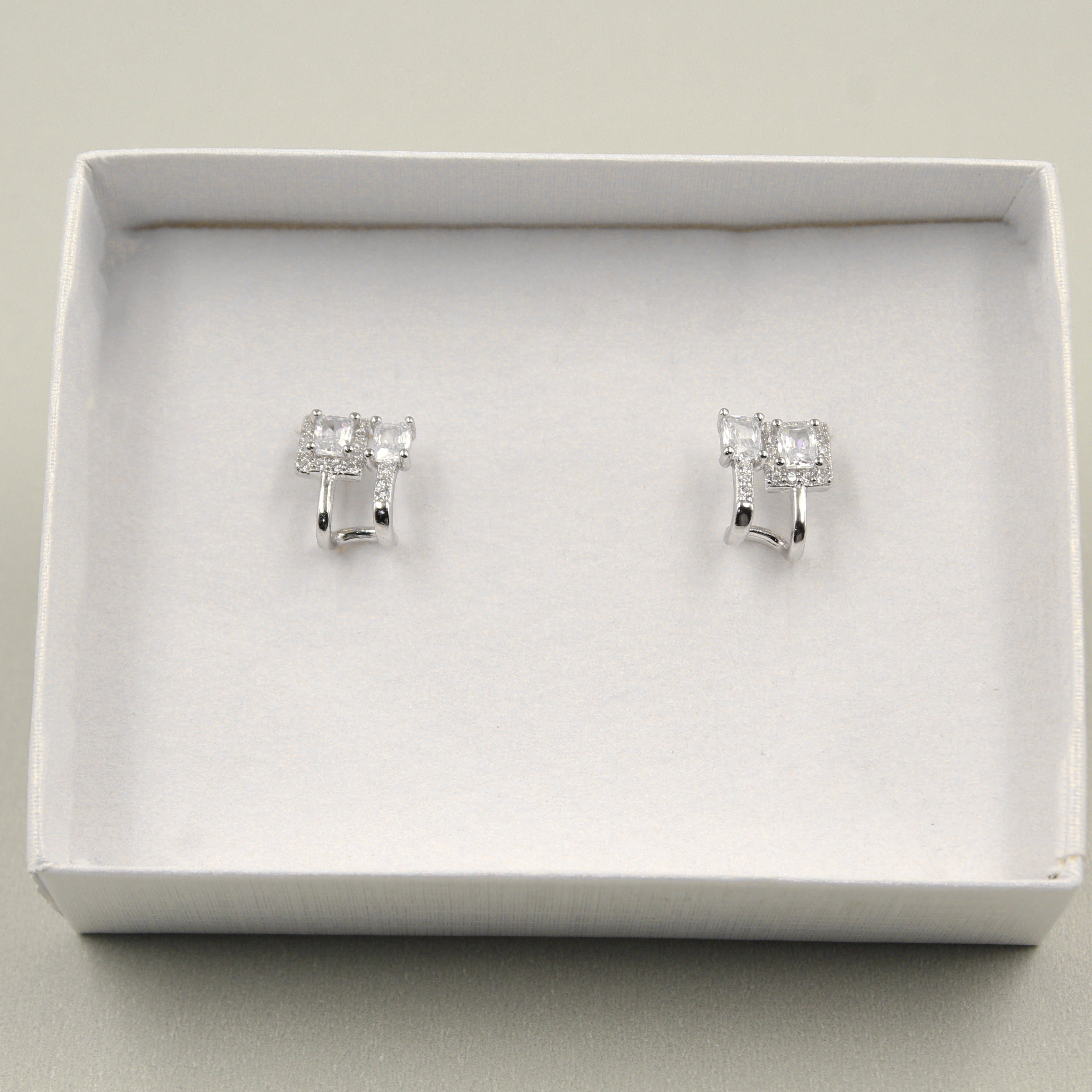 Par de aretes pequeños con diamantes rectangulares, presentados en una caja blanca.