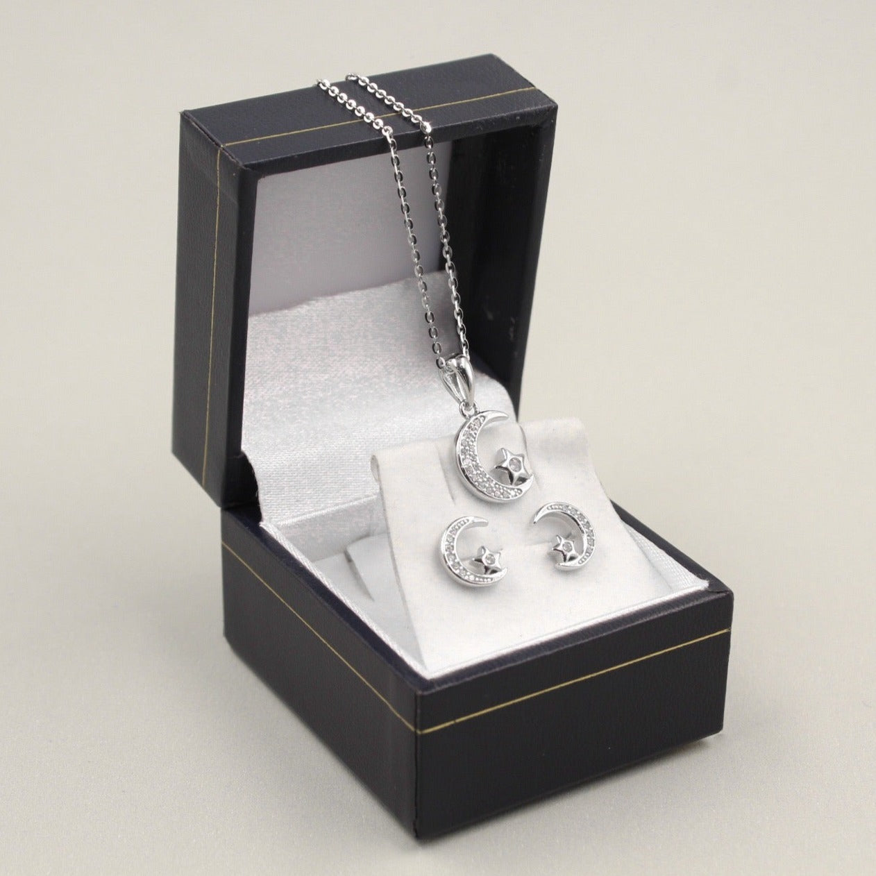 Juego de joyería con colgante y aretes en forma de flor, decorados con pequeños diamantes, presentados en una caja de joyería gris.